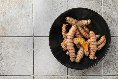 Bowl with raw turmeric roots on white tiled table, top view. Space for textの写真素材