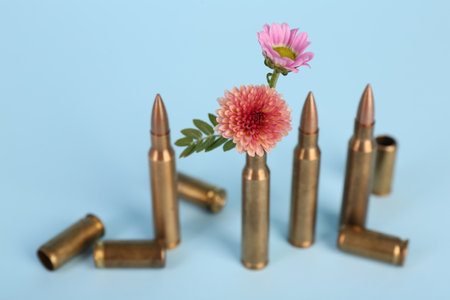 Bullets, cartridge cases and beautiful chrysanthemum flowers on light blue backgroundの写真素材