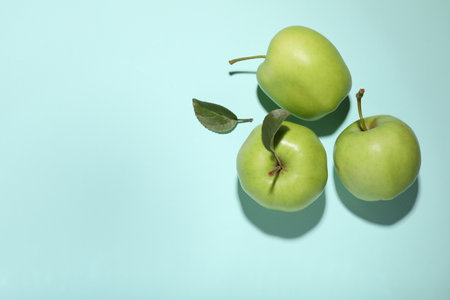 Fresh green apples on light blue background, flat lay. Space for text