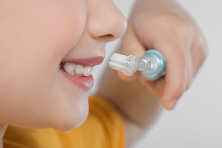 Girl brushing her teeth with electric toothbrush on light gray background, closeupの写真素材