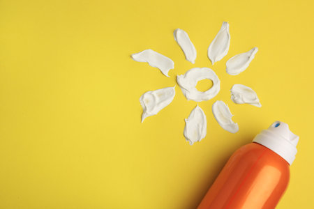 Drawing of sun and bottle with sunscreen on yellow background, top view and space for text. Skin...