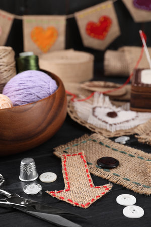 Pieces of burlap fabric with different stitches, scissors, threads, thimble and buttons on black table, closeupの写真素材