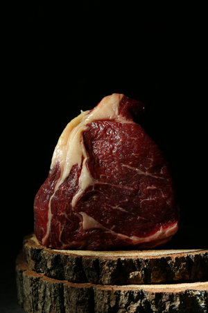 Piece of raw beef meat on decorative wooden stand against black background, closeupの写真素材
