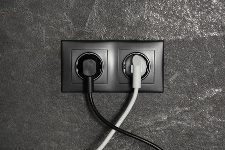 Power sockets with inserted plugs on dark gray wall. Electrical supply