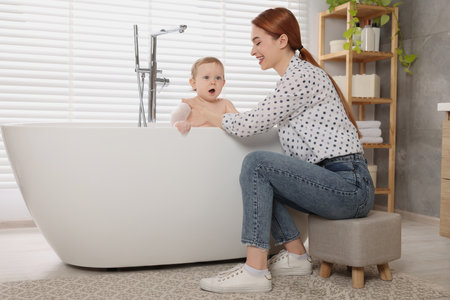 Mother washing her little baby in tub at home