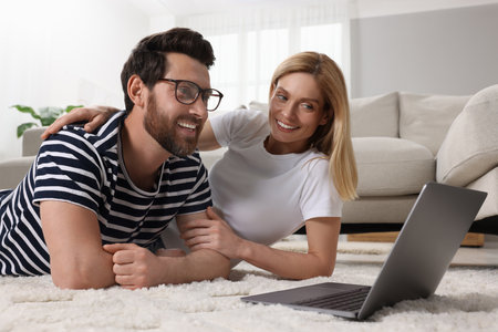 Happy couple with laptop on floor at homeの写真素材