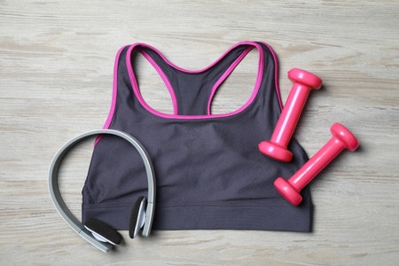 Stylish sports bra, dumbbells and headphones on wooden background, flat layの写真素材