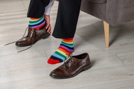 Man with colorful socks putting on stylish shoes indoors, closeupの写真素材