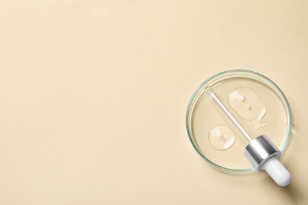 Petri dish with sample of cosmetic oil and pipette on beige background, top view. Space for textの写真素材