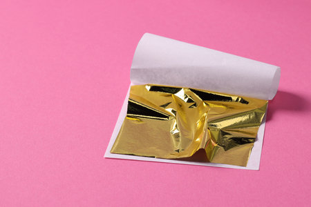 Edible gold leaf sheet on pink background, closeup. Space for textの写真素材