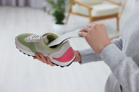 Woman putting orthopedic insole into shoe at home, closeup. Foot care