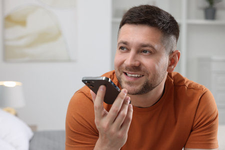 Handsome man recording voice message via smartphone at home