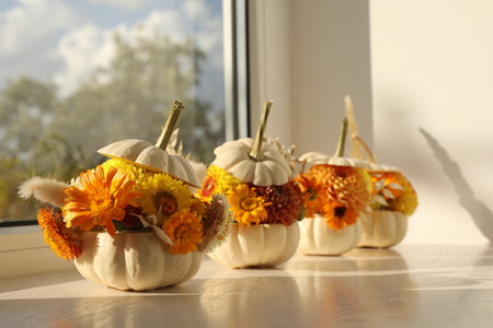Small pumpkins with beautiful flowers and spikelets on white wooden window sill indoorsの写真素材