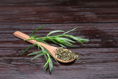 Spoon of dry tarragon and green leaves on wooden tableの写真素材