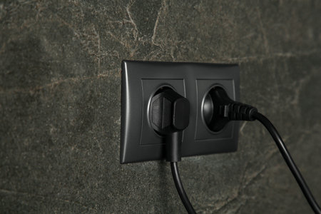 Power sockets with inserted plugs on dark gray wall, closeup. Electrical supply