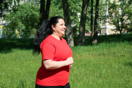 Overweight woman jogging in park on sunny dayの写真素材