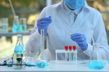 Scientist dripping sample into test tube in laboratory, closeup. Medical research