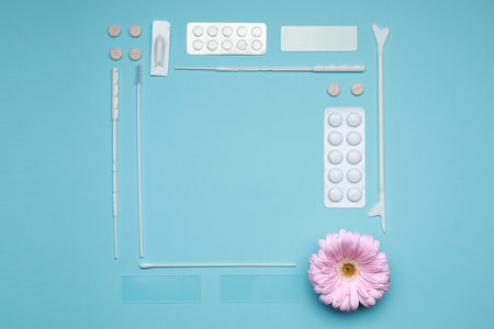 Frame of many gynecological pills, tools and gerbera flower on light blue background, flat lay....