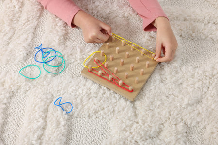 Motor skills development. Girl playing with geoboard and rubber bands on carpet, closeupの写真素材