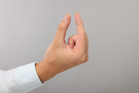 Man holding something in fingers on gray background, closeup. Space for textの写真素材