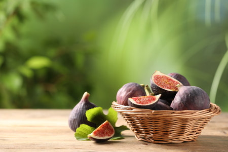 Wicker bowl with fresh ripe figs and green leaf on wooden table. Space for textの写真素材