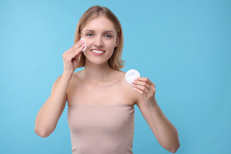 Young woman with cotton pads on light blue backgroundの写真素材