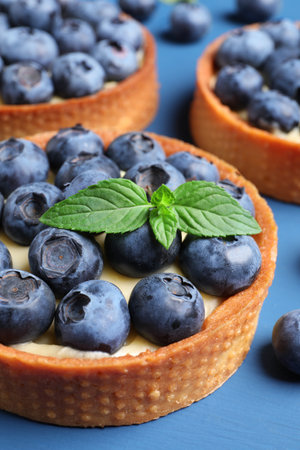 Tartlets with fresh blueberries and mint on blue table, closeup. Delicious dessertの写真素材