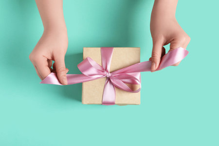 Woman tying bow of gift box on turquoise background, top viewの写真素材