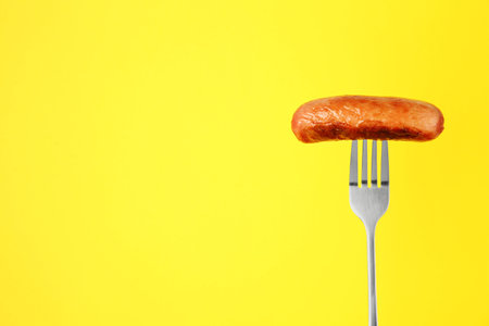 Fork with tasty fried sausage on yellow background. Space for textの写真素材