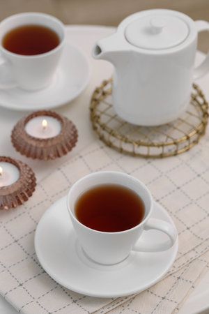 Cups of tea, teapot and burning candles on white tableの写真素材