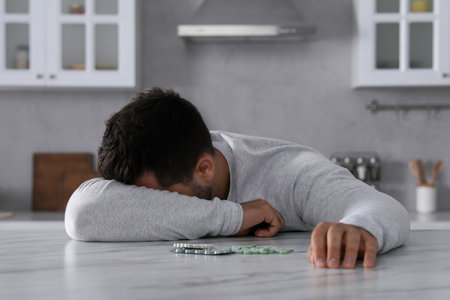 Man with antidepressant pills sleeping at white marble table in kitchenの写真素材