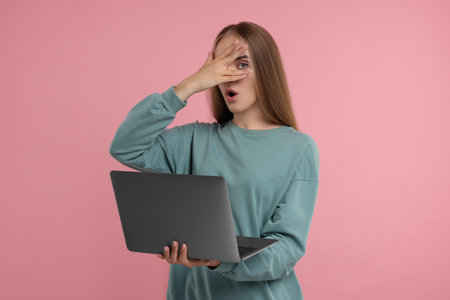 Embarrassed woman with laptop covering face on pink backgroundの写真素材
