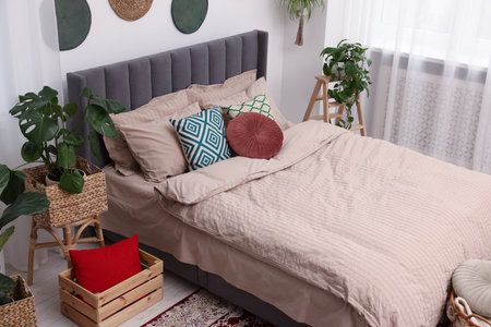 Large comfortable bed and potted houseplants in stylish bedroom. Interior design
