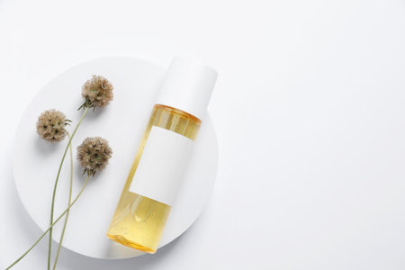 Bottle of cosmetic product, dried flowers and round podium on white background, top view. Space for textの写真素材