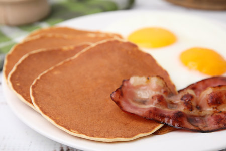 Tasty pancakes with fried eggs and bacon on white wooden table, closeupの写真素材
