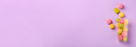 Plastic cup with color cotton balls on violet background, top view. Banner design with space for textの写真素材