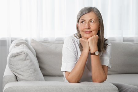 Portrait of beautiful senior woman on sofa at homeの写真素材
