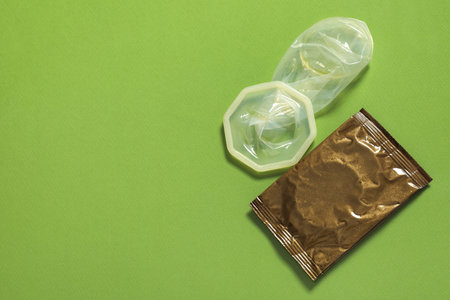 Unrolled female condom and package on green background, above view with space for text. Safe sexの写真素材