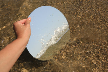 Woman reflecting sea and sky with round mirror on beach, closeupの写真素材