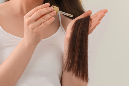 Woman applying essential oil onto hair on blurred background, closeupの写真素材