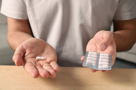 Man holding pills at wooden table, closeupの写真素材