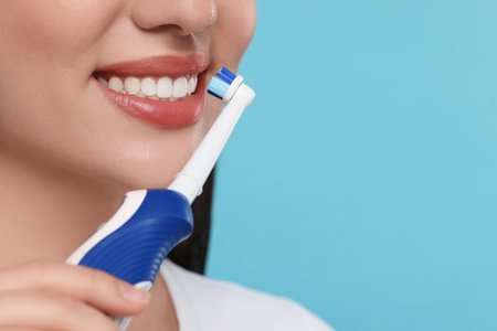 Woman brushing her teeth with electric toothbrush on light blue background, closeup. Space for textの写真素材