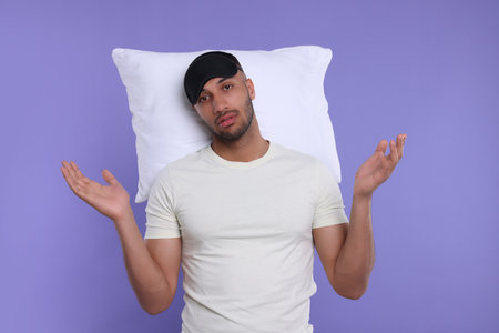 Tired man with pillow and sleep mask on violet background. Insomnia problemの写真素材
