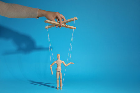 Woman pulling strings of puppet on light blue background, closeupの写真素材