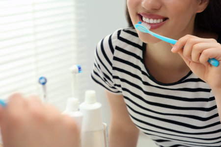 Woman brushing her teeth with plastic toothbrush near mirror in bathroom, closeupの写真素材