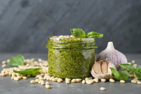 Jar of delicious pesto sauce and ingredients on gray table, closeupの写真素材