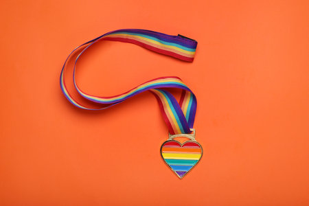 Rainbow ribbon with heart shaped pendant on orange background, top view. LGBT prideの写真素材