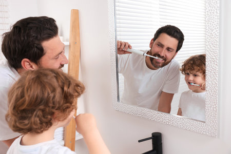 Father and his son brushing teeth together near mirror in bathroomの写真素材