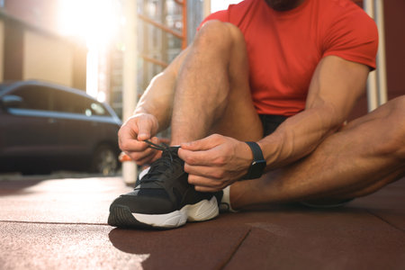 Man tying shoelaces before training at outdoor gym on sunny day, closeupの写真素材
