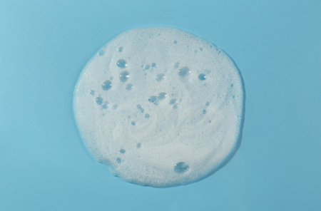 Sample of cleansing foam on light blue background, top view. Cosmetic product